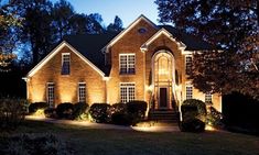 a house lit up at night with lights in the front yard and landscaping around it