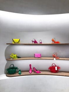 several shelves with different types of shoes and purses on them in front of a white wall