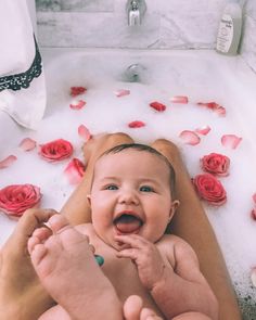 a woman holding a baby in a bathtub with rose petals on the floor next to it