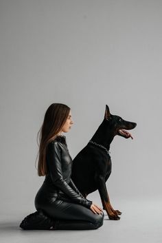 a woman is sitting on the floor with her dog, who is wearing a black leather outfit