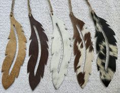 four different colored feathers hanging from a string on a white cloth covered surface, one is black, the other is brown and white