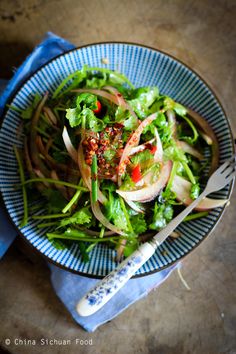 a blue bowl filled with salad on top of a wooden table next to a knife and fork