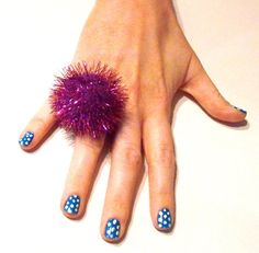 a woman's hand with blue and white polka dots on it, holding a purple pom - pom