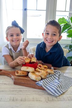 two young boys sitting at a table with bread and buns in front of them