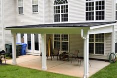 a covered patio with chairs and tables in front of a house