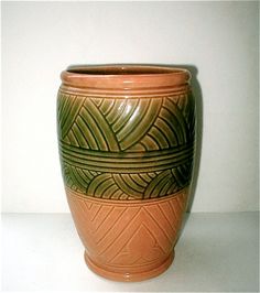 a brown and green vase sitting on top of a white table next to a wall