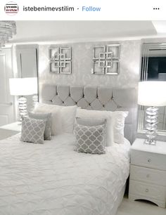 a white bed with four pillows and two lamps on either side of the headboard