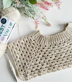 a crochet bag next to a ball of yarn and flowers on a table