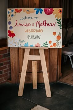 a welcome sign for a wedding with flowers on the front and back, sitting on a wooden easel