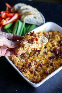 a hand holding a piece of pizza over a casserole dish