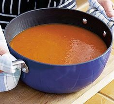 a blue pot filled with soup sitting on top of a wooden table next to a person