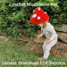 a young child wearing a red knitted mushroom hat playing with carrots in the grass