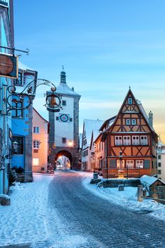 a snowy street with buildings on both sides and a clock tower in the background at sunset