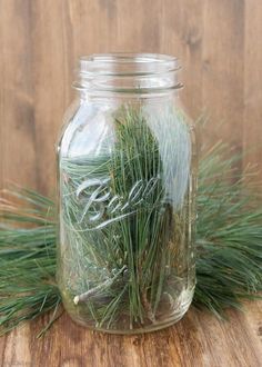 a glass jar filled with pine needles on top of a wooden table