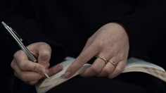 a person holding a pen and writing on an open book with two rings around their fingers