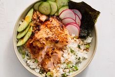 a bowl filled with rice, meat and veggies next to cucumbers