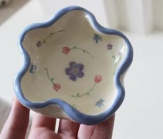 a hand holding a small bowl with flowers painted on the bottom and blue trim around the edge