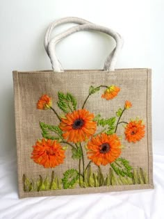 an embroidered bag with orange flowers on the front and green leaves on the back, sitting on a white surface