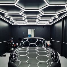 a car is parked in a black room with white lights on the ceiling and hexagonal design