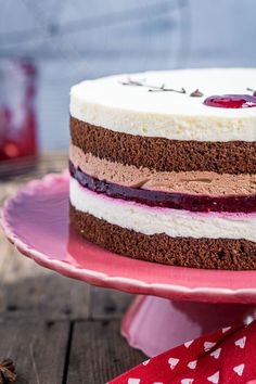 a cake on a pink plate topped with cherries and frosting, sitting on top of a wooden table