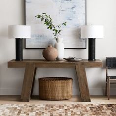 a table with two lamps and a basket on it in front of a large painting