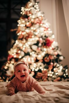 a baby laying in front of a christmas tree