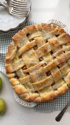 an apple pie is sitting on a plate next to some green apples and silverware