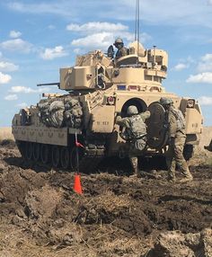 two men are standing in the mud next to an army tank with soldiers on it