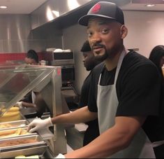 a man wearing an apron and hat in a kitchen with other people behind the counter