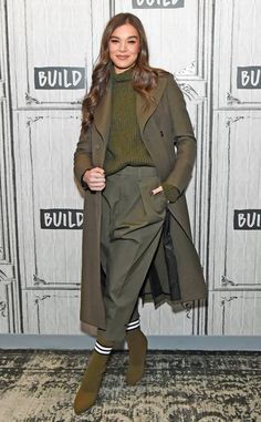 a woman standing in front of a white wall wearing a green coat and matching pants