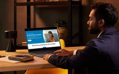 a man sitting in front of a laptop computer on top of a wooden desk next to a yellow chair