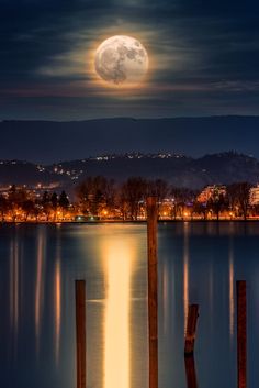 the full moon shines brightly in the night sky over a body of water with wooden docks