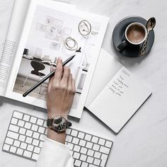 a person writing on a magazine next to a keyboard and cup of coffee with a pen