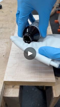 a person in blue gloves is sanding a piece of wood with a black bottle