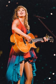 a woman holding a guitar while standing on top of a stage with a microphone in her hand