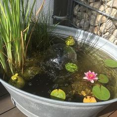 a large metal bowl filled with water and lily pads on top of a wooden deck