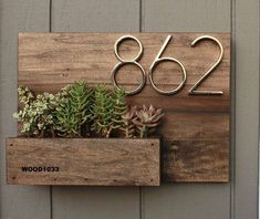 a house number sign with succulents in it on a wooden shelf next to a door