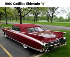 an old red car is parked on the side of the road in front of some trees