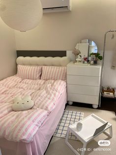 a bed with pink and white striped sheets in a small room next to a dresser