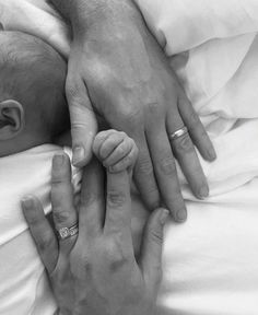 two adults holding a baby's hand in black and white