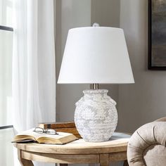 a white vase sitting on top of a wooden table next to a chair and lamp