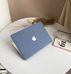 an apple laptop sitting on top of a white table next to a book and lamp