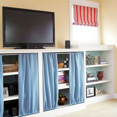 a flat screen tv sitting on top of a white book shelf next to a window