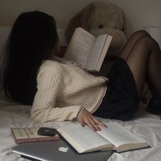 a woman is laying on her bed reading a book and holding an apple laptop computer