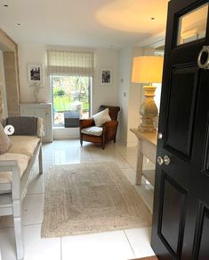 a living room filled with furniture and a large window next to a wooden door in front of a white tiled floor