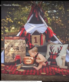 a baby sitting in front of a cake on top of a plaid cloth covered blanket