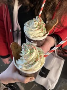 two people are holding up cupcakes with whipped cream and sprinkles