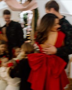 a woman in a red dress standing next to a group of people with their arms around each other