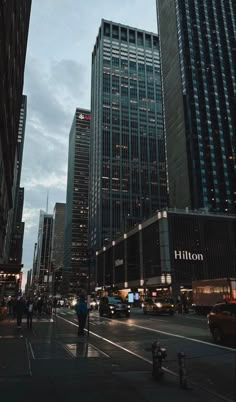 people are walking down the street in front of tall buildings at night time with lights on