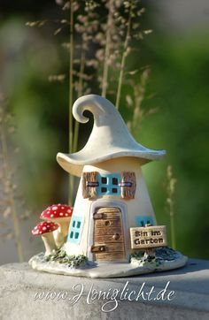 a small white house sitting on top of a stone wall next to tall grass and flowers